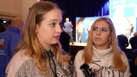 Two young women at an AfD rally talk to the BBC's Katya Adler