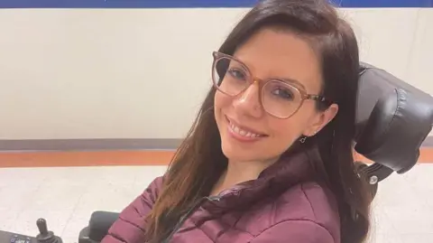 Dentsu Breanna in her wheelchair, looking at the camera and smiling.