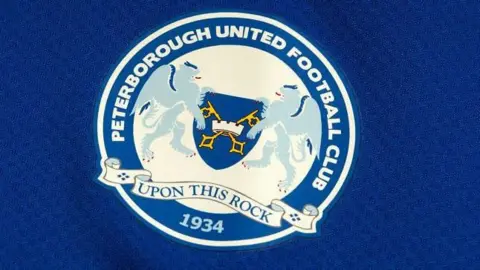 Getty Images Peterborough United's previous club crest, featuring lions, cross keys, the motto "UPON THIS ROCK" and "1934", on a blue background.