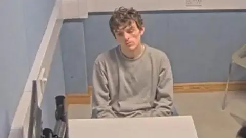 Essex Police Dominic Boultwood sitting behind a white table in an interview room.