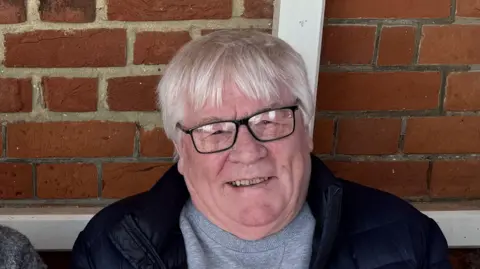 George King/BBC A close-up head and shoulders shot of Roy Day - an elderly man with white hair and glasses. He is looking directly into the camera