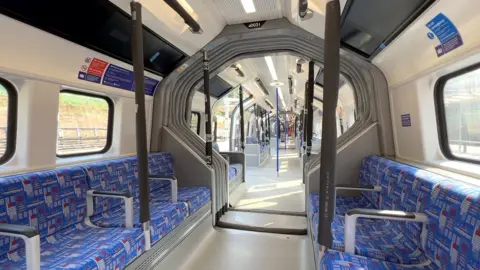 A train carriage with seating on either side which goes through to another carriage with no doors.
