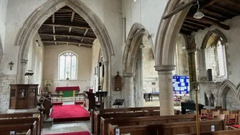 Peter Slinger Inside St Andrew's Church are rows of wooden pews, stone arches and a wooden roof. There is a red carpet in front of the altar and in the aisle