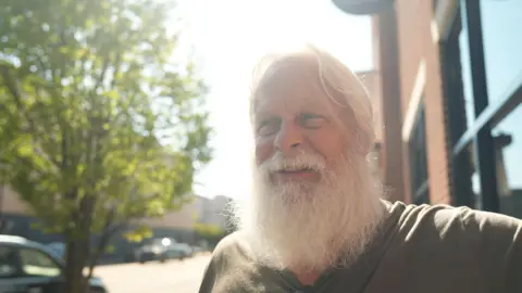 David Carter sports a full white beard - which helps him play Santa at Christmas - as he stands on a main street in downtown Kingstport