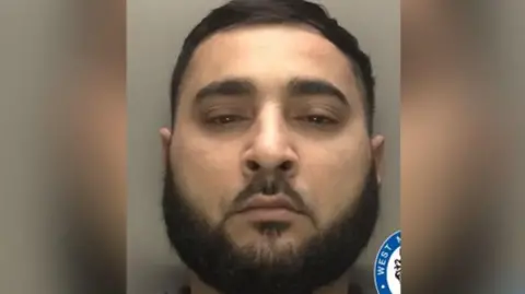 Police handout Mohammed appears in a police mugshot photo. He has dark hair and a beard and is staring directly at the camera.