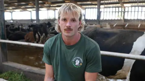 A man with long blonde hair and a moustache wearing a green t shirt