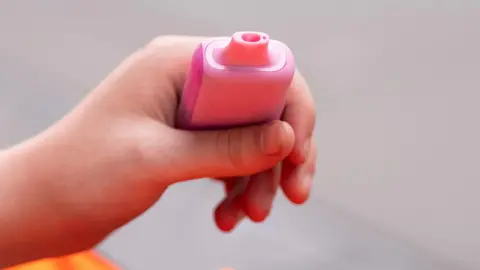 A hand holding a pink disposable vape