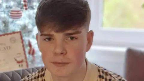 Police Scotland Kayden Moy looks in the camera and smiles - he has short dark hair and wears a checked polo shirt.