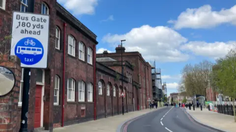 A sign to the left-hand side of the picture, in front of a row of buildings. The sign says bus gate 180 yards ahead.