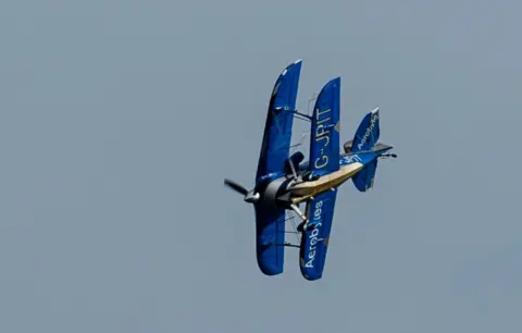 Bold Media Agency A blue Pitts bi-plane bearing the callsign G-JPIT performing a steep turn in the sky