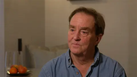 Jim Steyer from Common Sense Media is wearing an open-collared demim shirt and sitting into a muted-coloured room next to a plate of whole fruit. He has short brown hair with a side parting.