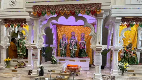 Three deities draped in green dresses, sitting inside a white marble arch, located inside the Temple room. There are few more deities in separate marble arches places across the room.