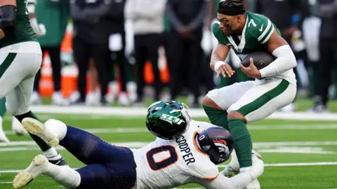 PA Media An American footballer wearing green is tackled by one wearing white