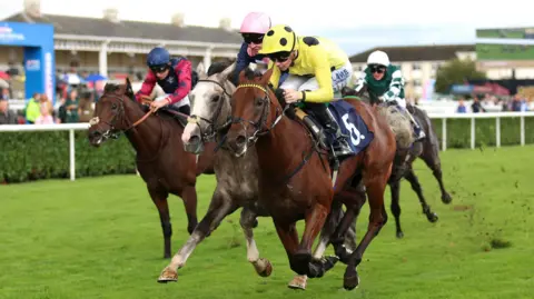 PA Media Three jockeys riding horses at a racecourse