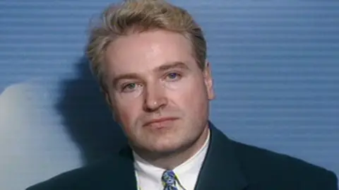 BBC Neil Foden as a young man depicted against a blue background and wearing a dark suit and blue tie