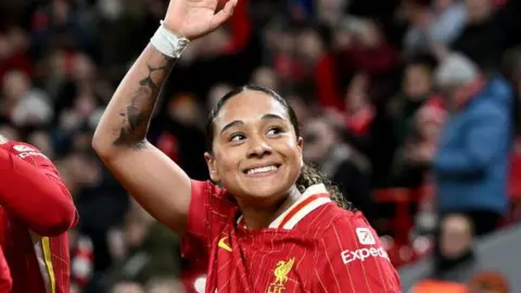Olivia Smith waves as she wears Liverpool match kit