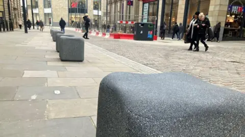 LDRS Stones in the shape of cubes on a street in Bradford are to be used as seats. Image shows road works on a shopping street and people walking around. 