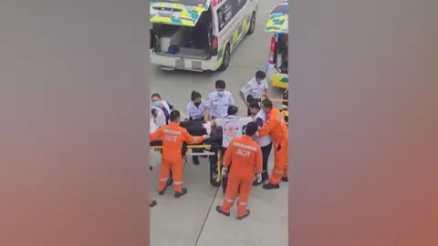 Emergency services dressed in orange overalls attend the injured person on a stretcher