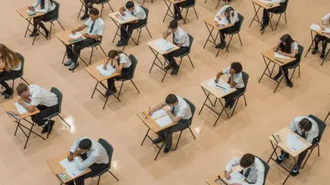 Getty Students sitting their exams, taken from above in an aerial view. They are wearing shirts and ties and sitting at individual desks, writing their exam papers.