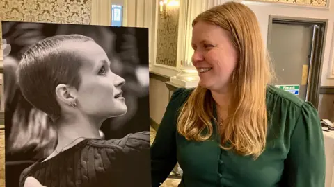 BBC/Nicola Rees Mum Vicky Robayna, who has mid-length blonde hair, looks at a large black and white photograph of her teen daughter Liz Hatton.