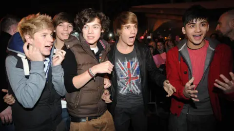 PA Media One Direction, while they were on ITV's X Factor show in 2010, are greeted by excited fans at a Bradford music shop. Left to right: Niall Horan, Louis Tomlinson, Harry Styles, Liam Payne and Zayn Malik.