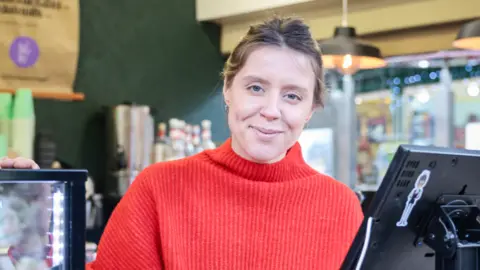 Kenny Brown Marta Biegaj, wearing a red jumper, smiles as she works behind the till on her stall