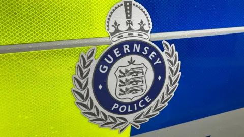 BBC Guernsey Police crest on a background with reflective fluorescent yellow on the left and reflective blue on the right