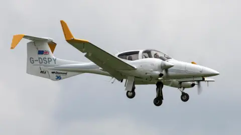 The Diamond DA42 MPP twin engine light aircraft G-DSPY on approach to land at Waddington. It is white with yellow wing tips.