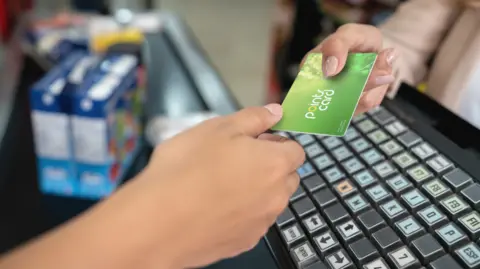 Getty Images Customer hands over loyalty card to cashier in shop