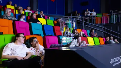 Adults and children sat on colourful cinema seats watching a movie screen