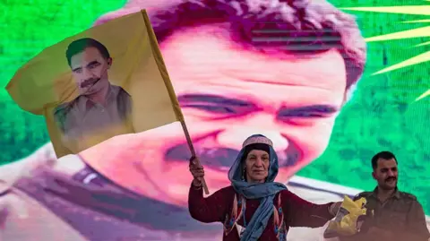 A supporter holds a flag with the face of Abdullah Ocalan, with his face also on the backdrop behind her