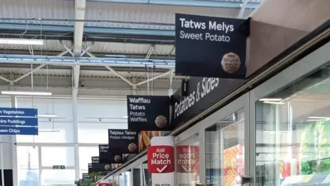 Another frozen aisle in Helston Tesco. The sign reads 'tatws melys', and underneath, 'sweet potato'. Other signs read 'wafflau tatws' or potato waffles. 