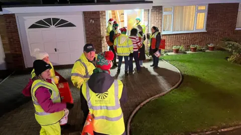 Whittlesey Roundtable Volunteers wearing a high-visibility green jacket standing on a drive way 