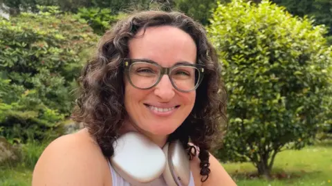 Lady, with brown curly hair wearing glasses, and headphones around her neck.