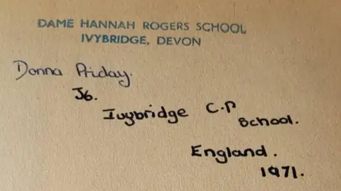 Nicola Lomax A close up of the front blank page of the book which has a blue stamp which said "DAME HANNAH ROGERS SCHOOL IVYBRIDGE, DEVON". Below it written in a black ink "Donna Priday, J6. Ivybridge C.P School, England. 1971. 