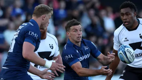 Sale's George Ford passing the ball to Dan du Preez with two Bristol players in attendance