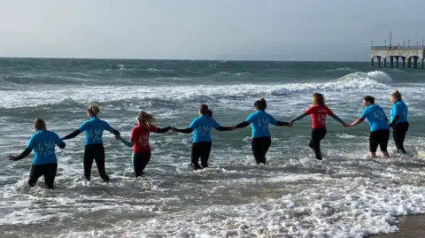 Dorset Community Foundation A group of people stood knee high in the sea facing backwards, with a pier in the background