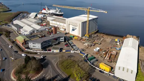 A drone shot of a shipyard with a large ship moored in the background