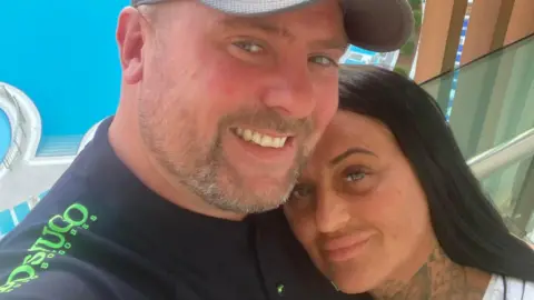 A man and woman hugging and smiling at the camera in front of a swimming pool