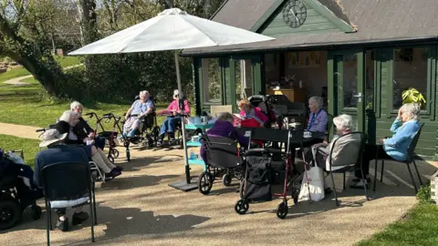 Contributed Residents at a care home enjoying some outdoor time. They are all sitting in chairs and under shade on a sunny day.