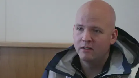 Jack Dowden, who is wearing a navy coat and Crosby Wombles safety vest, is staring off camera in this candid image. 