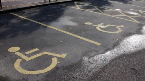 Car park featuring spaces marked in yellow paint with the wheelchair symbol.