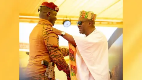  Capt Ibrahim Traore wearing military fatigues and with a holstered pistol, greets President John Mahama.