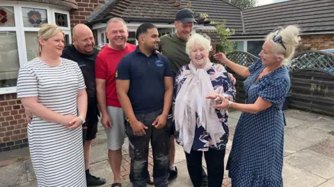 Four men and one woman smile with Wright and Day in a photo taken at the front of the house