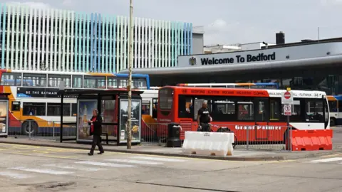 Getty A wide angle shot of Bedford bus station with lots of buses parked and a person crossing the road to the left of the shot.