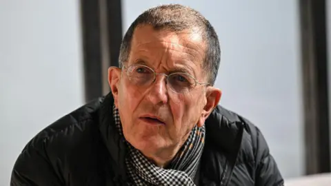 Getty Images A close-up image of Sir Antony Gormley. He has short dark hair and is wearing wire-rimmed glasses, a black jacket and a checked scarf.