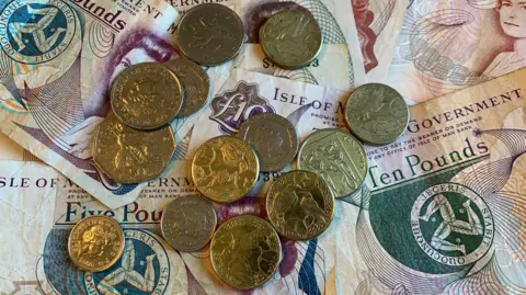 An assortment of Manx 10 and five pound notes, with a collection of coins on top of them - a mixture of pound coins, and small change.
