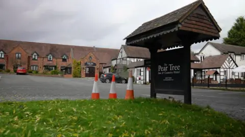 The Pear Tree Inn & Country Hotel sign. A red brick building in the distance and white and black buildings in the middle and on the right.
