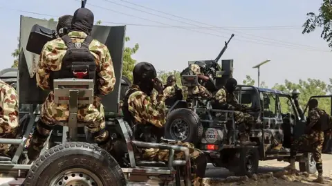 Nigerian soldiers seated in trucks, wearing military camouflage uniform and wearing black hood