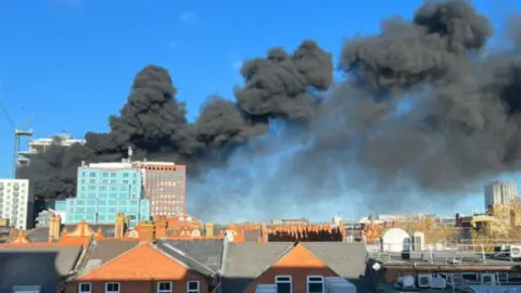 Robert Bunting Black smoke billows across the blue sky over Reading.